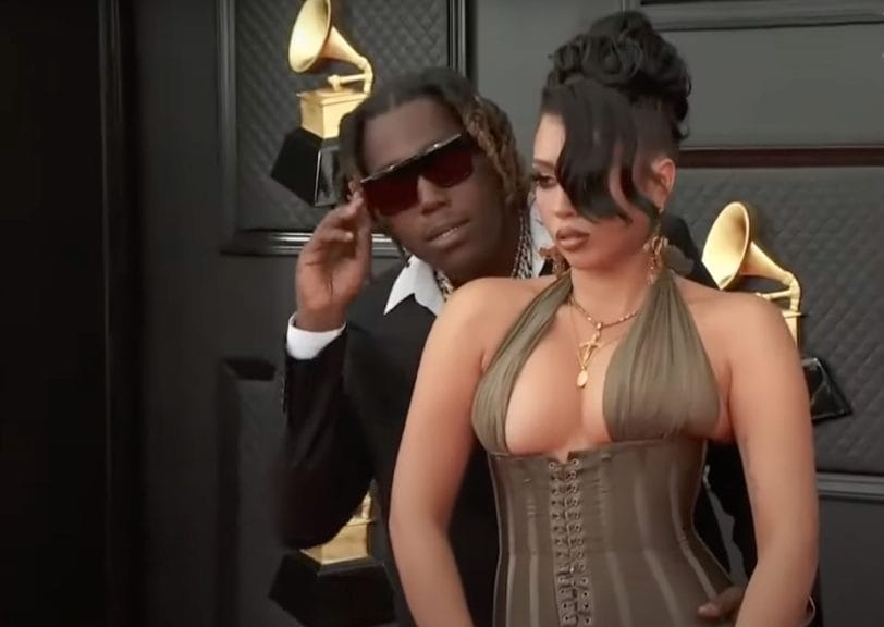 Kali Uchis with her boyfriend, Don Toliver at the 64th Grammys. Kali Uchis has her hair in a bun with a front piece hanging over her eye wearing a tight-fitted green dress. Don Toliver is wearing a black suit with sunglasses.